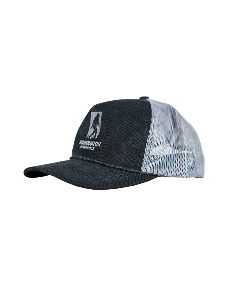 Side angle of black Sasquatch Controls embroidered corduroy trucker hat.
